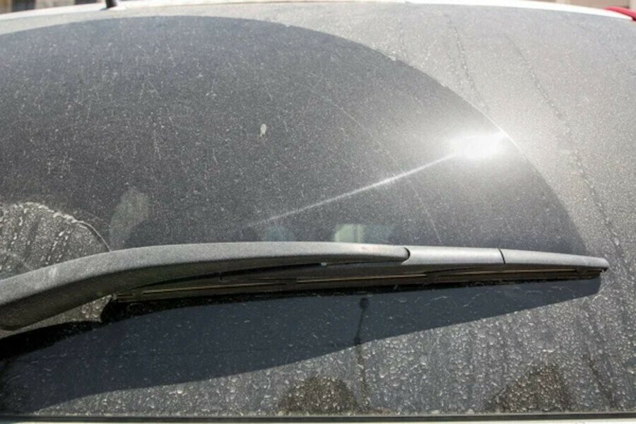 Неочищенное заднее стекло машины, щётка и само стекло в пыли